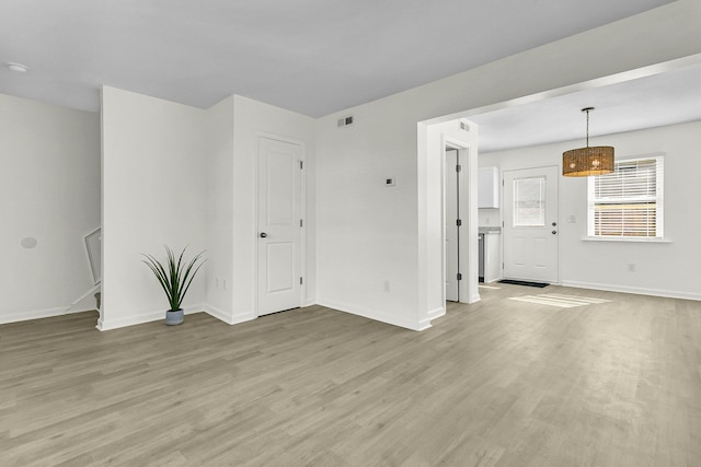 unfurnished living room with visible vents, baseboards, light wood-style floors, and stairs