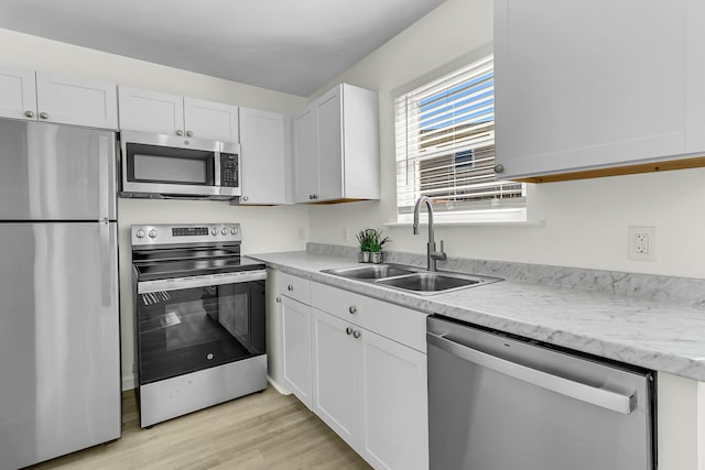 kitchen featuring a sink, light countertops, appliances with stainless steel finishes, white cabinetry, and light wood-type flooring