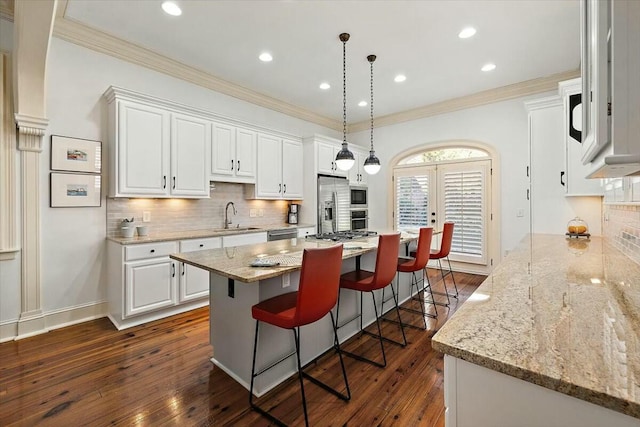 kitchen featuring hanging light fixtures, appliances with stainless steel finishes, a kitchen island, white cabinets, and backsplash