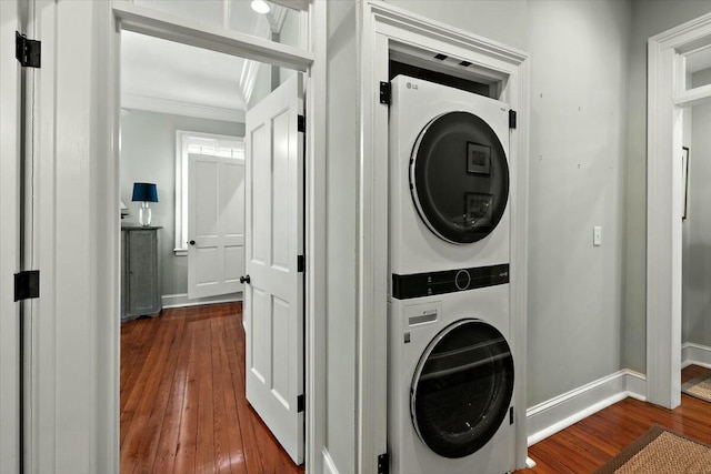 clothes washing area featuring dark wood-type flooring, stacked washer / drying machine, and crown molding