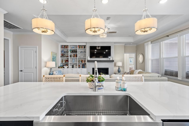 kitchen with light stone counters, ornamental molding, a raised ceiling, and hanging light fixtures