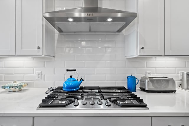 kitchen with tasteful backsplash, wall chimney range hood, stainless steel gas cooktop, and white cabinets