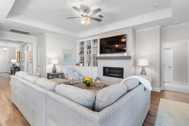 living room featuring crown molding, ceiling fan, wood-type flooring, and a tray ceiling