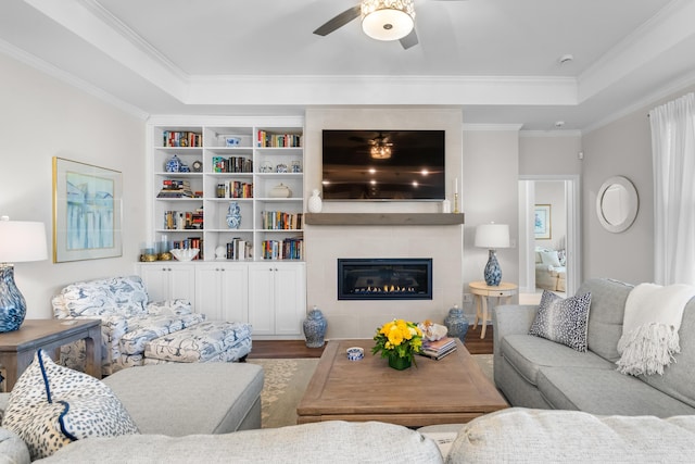 living room with a large fireplace, ornamental molding, a raised ceiling, ceiling fan, and hardwood / wood-style floors