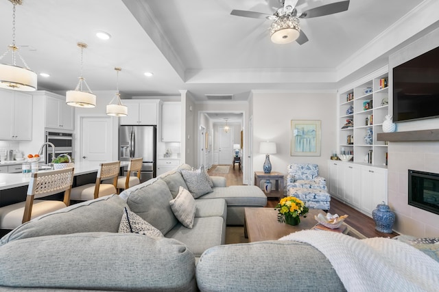 living room with crown molding, a tile fireplace, ceiling fan, dark hardwood / wood-style floors, and a raised ceiling