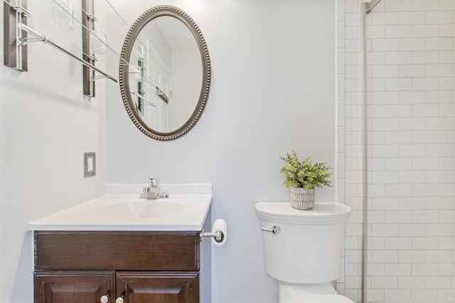 bathroom featuring toilet, a tile shower, and vanity