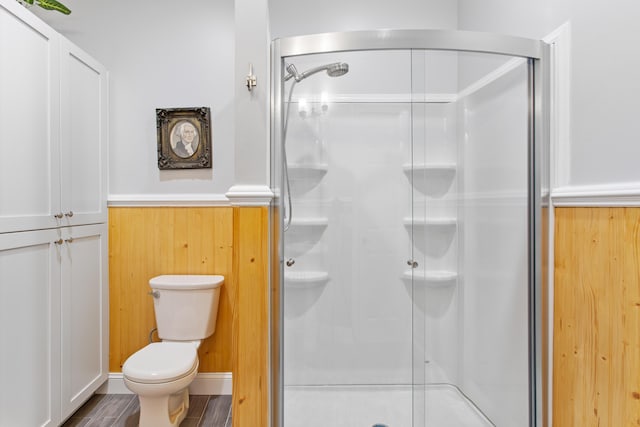 bathroom with a stall shower, a wainscoted wall, toilet, and wood finished floors