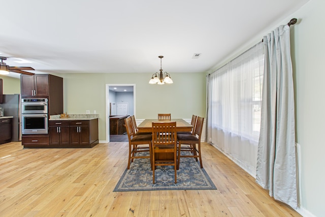 dining room with ceiling fan with notable chandelier, light wood-type flooring, visible vents, and baseboards