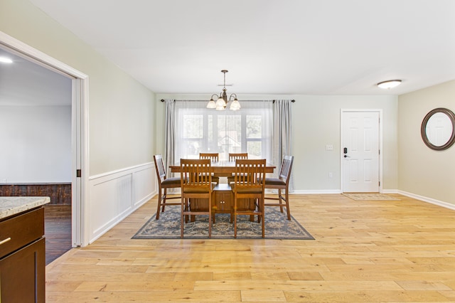 dining space featuring a wainscoted wall, light wood-style flooring, and a notable chandelier