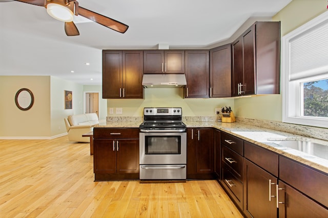 kitchen with light wood finished floors, baseboards, stainless steel electric range oven, light stone countertops, and under cabinet range hood