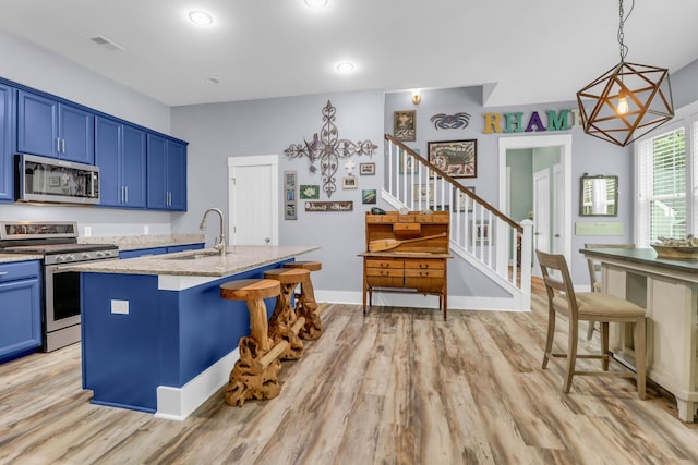 kitchen with appliances with stainless steel finishes, a sink, blue cabinets, light stone counters, and light wood-style flooring