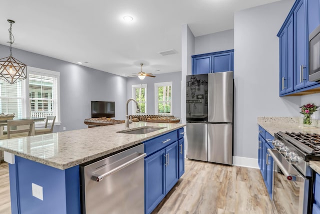 kitchen with appliances with stainless steel finishes, a sink, blue cabinets, light wood finished floors, and a center island with sink
