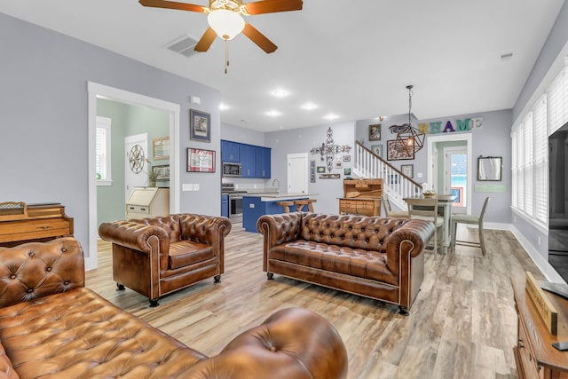 living room with stairway, light wood-type flooring, a ceiling fan, and baseboards