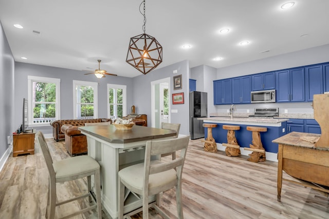 kitchen with appliances with stainless steel finishes, blue cabinets, light wood-type flooring, an island with sink, and recessed lighting