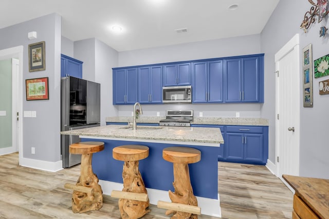 kitchen with appliances with stainless steel finishes, blue cabinetry, a sink, and light wood-style flooring