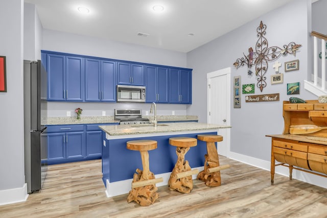 kitchen with appliances with stainless steel finishes, blue cabinetry, light wood-style floors, and light stone counters