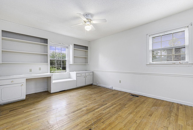 unfurnished office with a textured ceiling, built in desk, light hardwood / wood-style floors, and ceiling fan