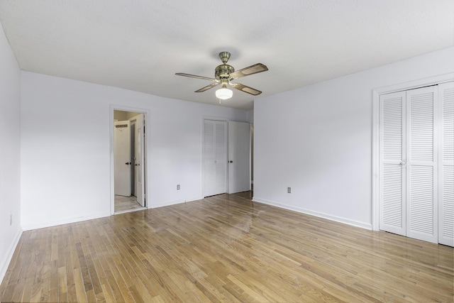 unfurnished bedroom featuring ceiling fan, light hardwood / wood-style floors, and multiple closets