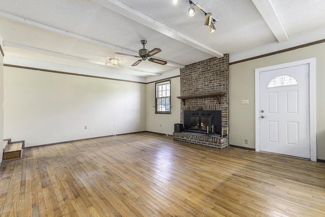 unfurnished living room with a brick fireplace, a textured ceiling, ceiling fan, beam ceiling, and light hardwood / wood-style floors