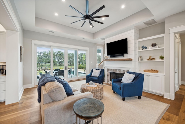 living room with light wood-type flooring, a fireplace, and a raised ceiling