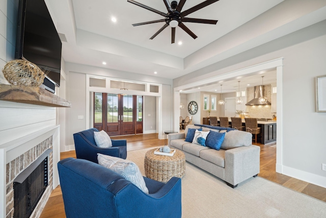 living room with french doors, a tray ceiling, light wood-type flooring, and baseboards