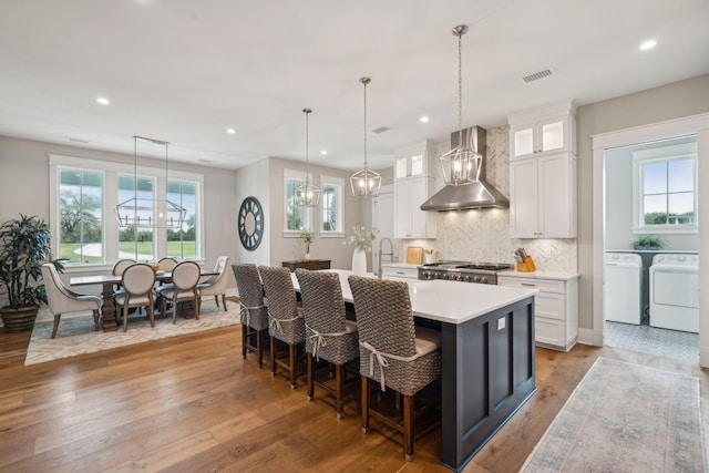 kitchen featuring wall chimney range hood, white cabinetry, glass insert cabinets, and light countertops