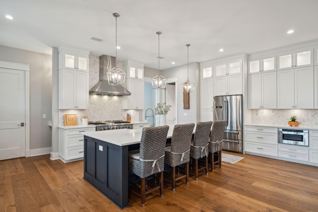 kitchen featuring white cabinets, high quality fridge, glass insert cabinets, light countertops, and wall chimney range hood