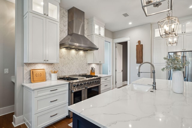 kitchen featuring white cabinetry, wall chimney exhaust hood, appliances with stainless steel finishes, and glass insert cabinets