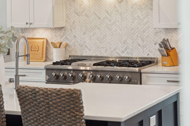 kitchen featuring light stone countertops, white cabinetry, backsplash, and stainless steel stove