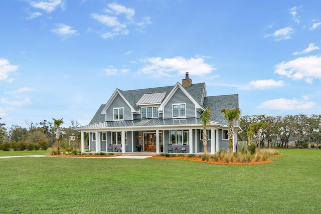 country-style home with a chimney, covered porch, a standing seam roof, metal roof, and a front lawn