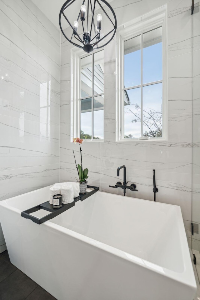 full bathroom featuring plenty of natural light, a soaking tub, tile walls, and an inviting chandelier