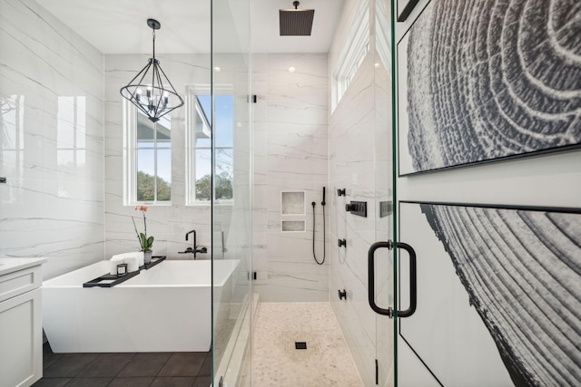 bathroom featuring a marble finish shower, an inviting chandelier, a freestanding bath, vanity, and tile walls