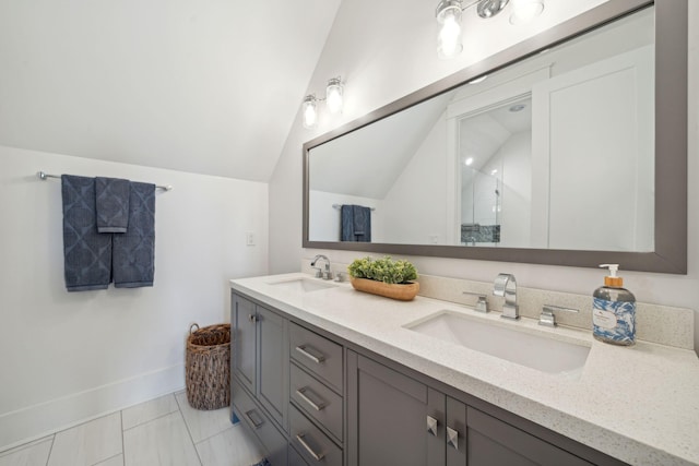 full bath with double vanity, baseboards, vaulted ceiling, and a sink