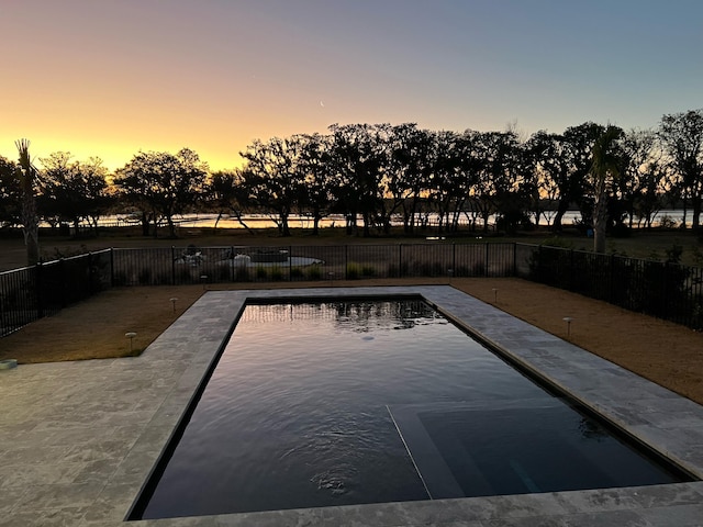 pool at dusk featuring a patio area and fence