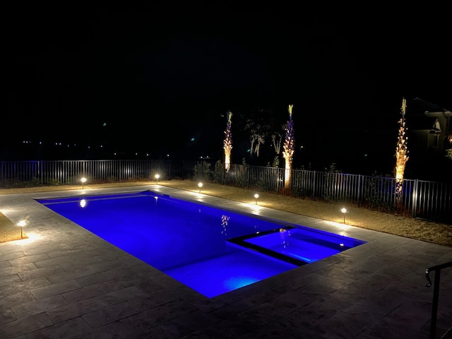 pool at twilight featuring a fenced backyard and an in ground hot tub