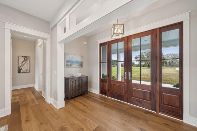 doorway to outside featuring baseboards, french doors, light wood-type flooring, and an inviting chandelier