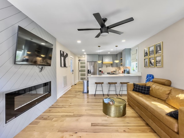 living room featuring sink, a fireplace, light hardwood / wood-style floors, and ceiling fan