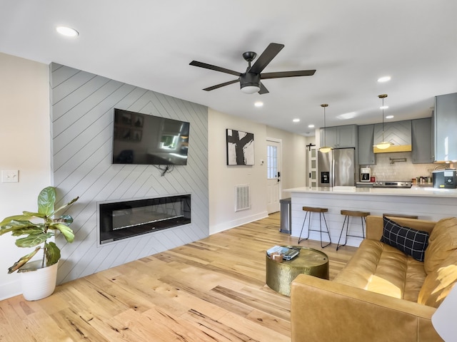 living room with ceiling fan, a large fireplace, and light wood-type flooring