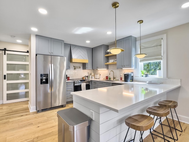 kitchen with a breakfast bar area, appliances with stainless steel finishes, hanging light fixtures, kitchen peninsula, and a barn door