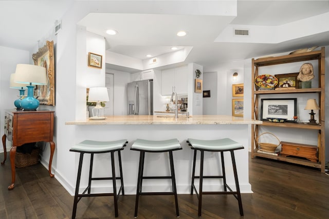 kitchen with white cabinetry, stainless steel fridge, a kitchen bar, and kitchen peninsula