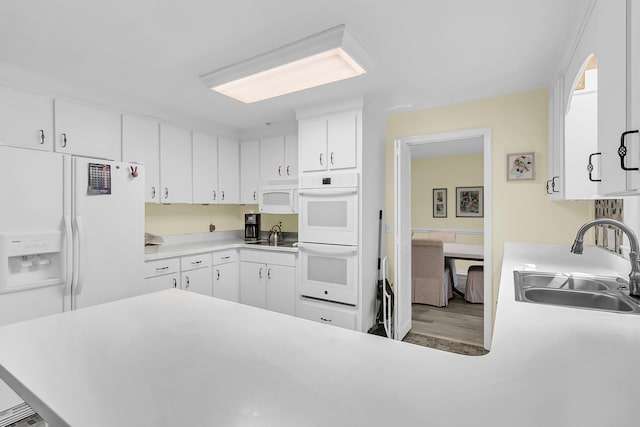 kitchen with white appliances, a sink, white cabinetry, light countertops, and wood finished floors