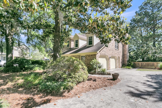 view of home's exterior featuring driveway, brick siding, a garage, and fence