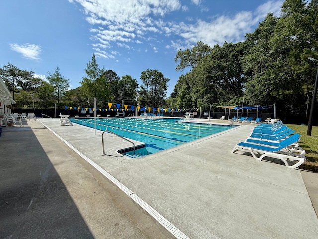 community pool featuring a patio, view of wooded area, and fence