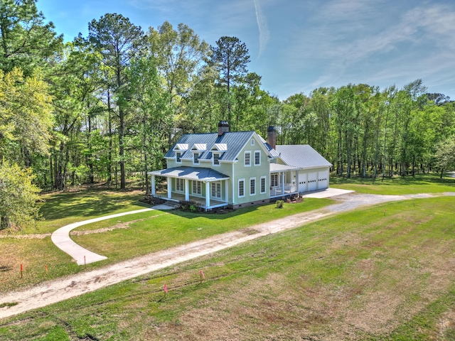 view of front of house with a chimney, driveway, an attached garage, a front yard, and metal roof