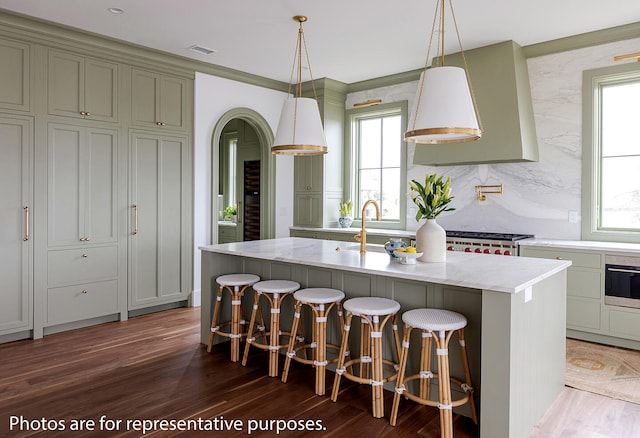 kitchen featuring dark wood-type flooring, a wealth of natural light, a kitchen bar, and a kitchen island with sink