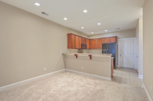 kitchen featuring black appliances, light colored carpet, kitchen peninsula, and a kitchen bar