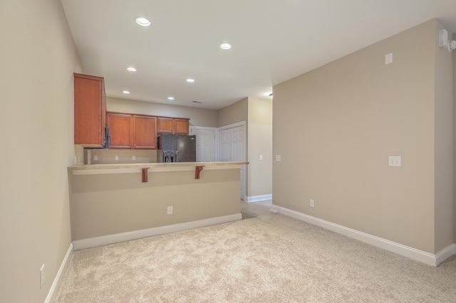 kitchen featuring a kitchen breakfast bar, light colored carpet, black fridge, and kitchen peninsula