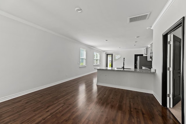 unfurnished living room featuring a sink, ornamental molding, dark wood-style floors, and baseboards