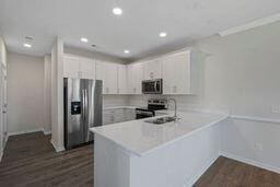 kitchen with sink, appliances with stainless steel finishes, dark wood-type flooring, kitchen peninsula, and white cabinets