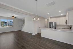 kitchen with white cabinetry, ceiling fan with notable chandelier, kitchen peninsula, stainless steel fridge, and dark wood-type flooring